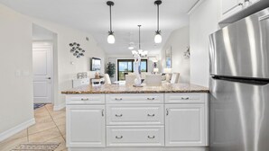 Een moderne keuken met witte kasten, een roestvrijstalen koelkast en hangende verlichting.