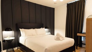 A neatly made bed with white linens, a black headboard, and a small round table with a lamp beside it. - Sosuite | 2BR Apt w W/D, Newly renovated (Philadelphia)