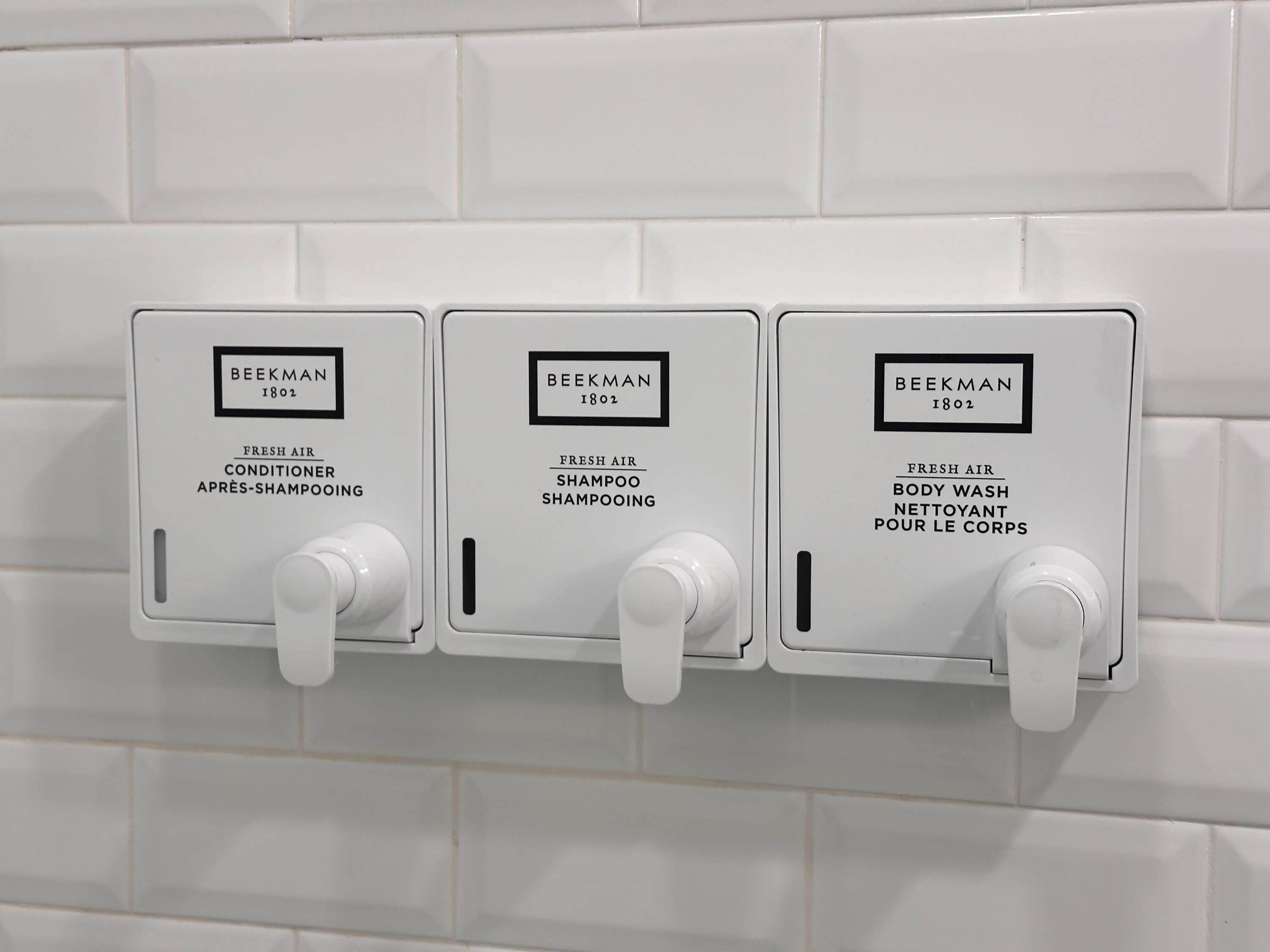 Tres dispensadores montados en la pared con la etiqueta 'BEEKMAN 1802' para aire acondicionado, champú y gel de baño.