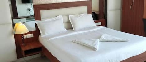 A neatly made bed with white linens and pillows, a bedside lamp, a wooden nightstand, and a mirror above the bed.
