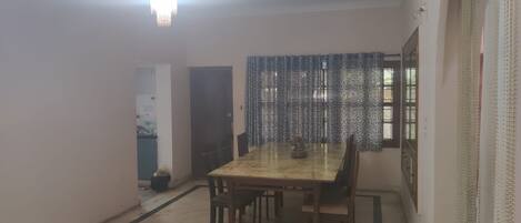A dining room with a large table and chairs, a chandelier, patterned curtains, and a view of the outdoors.