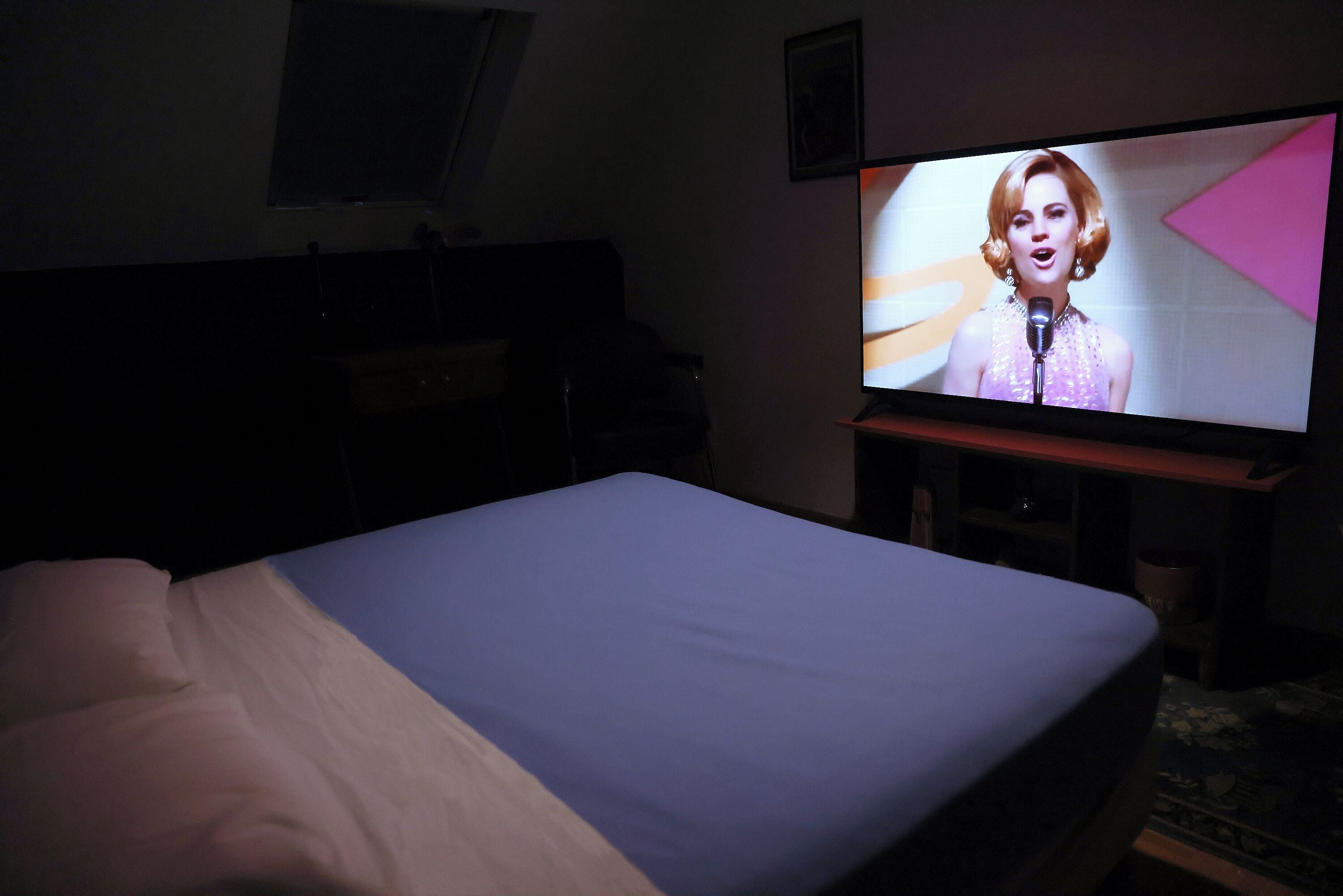 A hotel room with a bed, a television on a stand, and a wall-mounted picture.