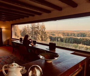 A room with a large window overlooking a forested landscape, a wooden table with a laptop, and a kettle on the table. - Domaine Foray (Villecien)
