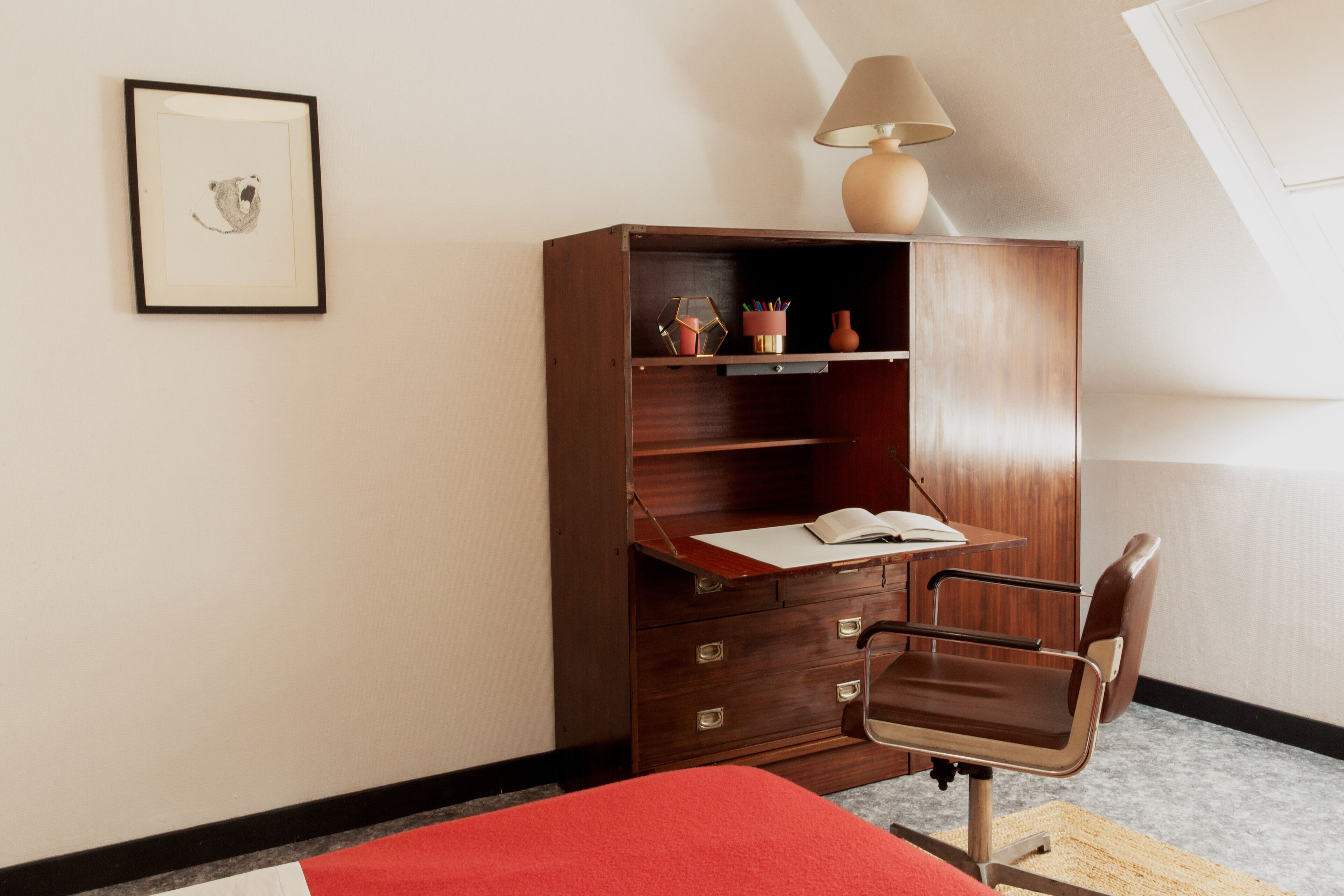 Un salón de estudio con un escritorio de madera, una silla, una lámpara y un cuadro en la pared.