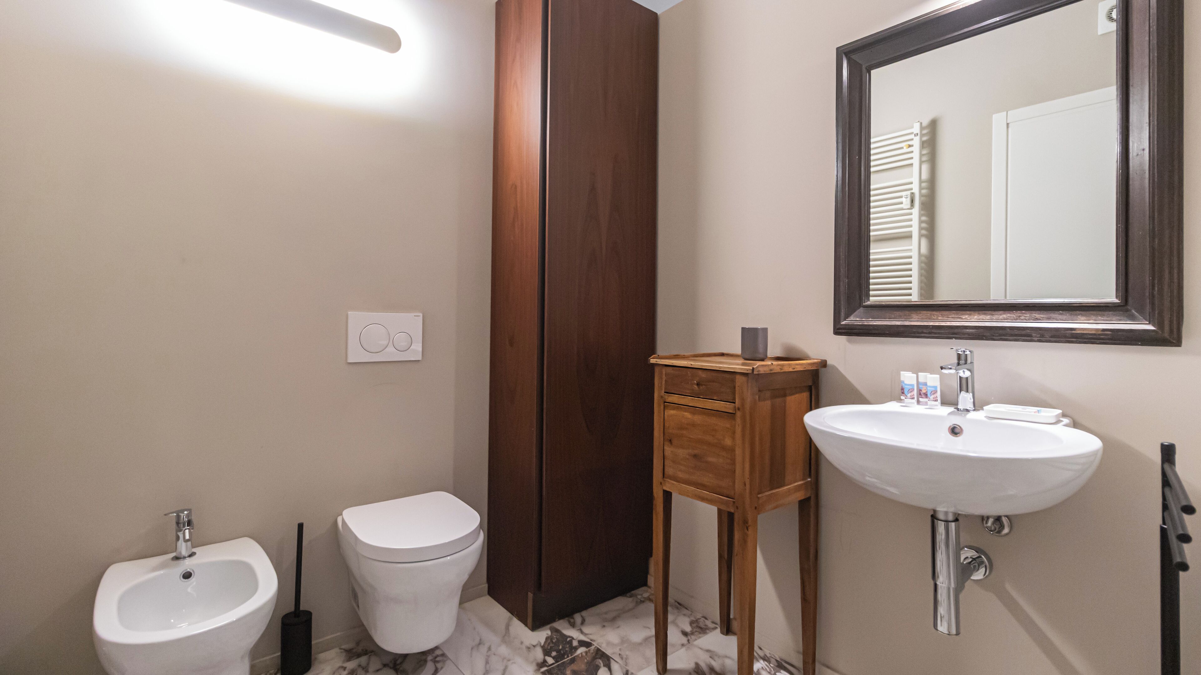 A bathroom with a toilet, bidet, sink, mirror, and a wooden cabinet.