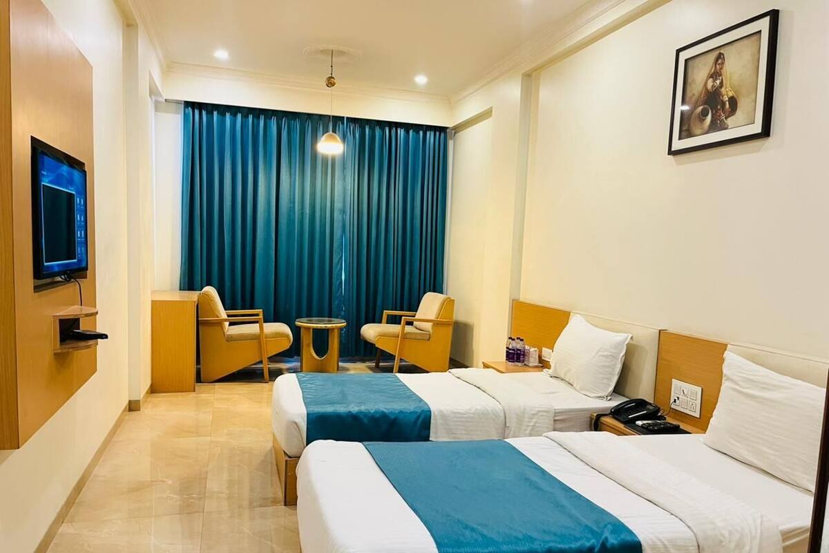 A hotel room with two beds, a TV, a desk, a chair, and a blue curtain.