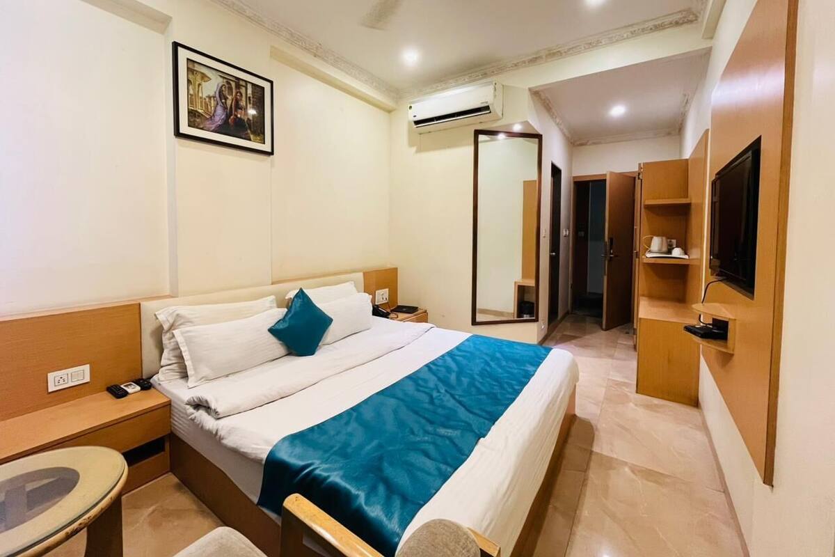 A hotel room with a bed, bedside table, nightstand, and a television mounted on the wall.