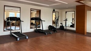 A gym with treadmills, elliptical machines, and exercise bikes, large mirrors on the walls, and a wooden floor. - The gorbandh palace (Ankleshwar)