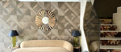 A modern living room with a geometric patterned wallpaper, a round mirror, and a staircase with a pixelated design.