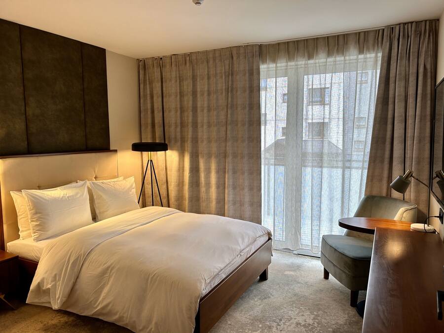 Hotelkamer met een groot bed, een bureau, een stoel, een vloerlamp en uitzicht op een gebouw.