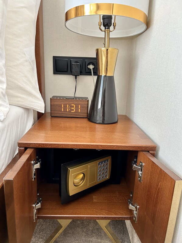 Une table de chevet en bois avec une lampe, une horloge et un coffre-fort.