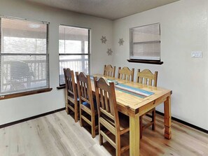 Une salle à manger avec une table et des chaises en bois, de grandes fenêtres équipées de stores et un plancher de couleur claire.