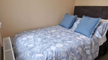 A single bed with a floral bedspread, a dark headboard, and a wall-mounted air vent.