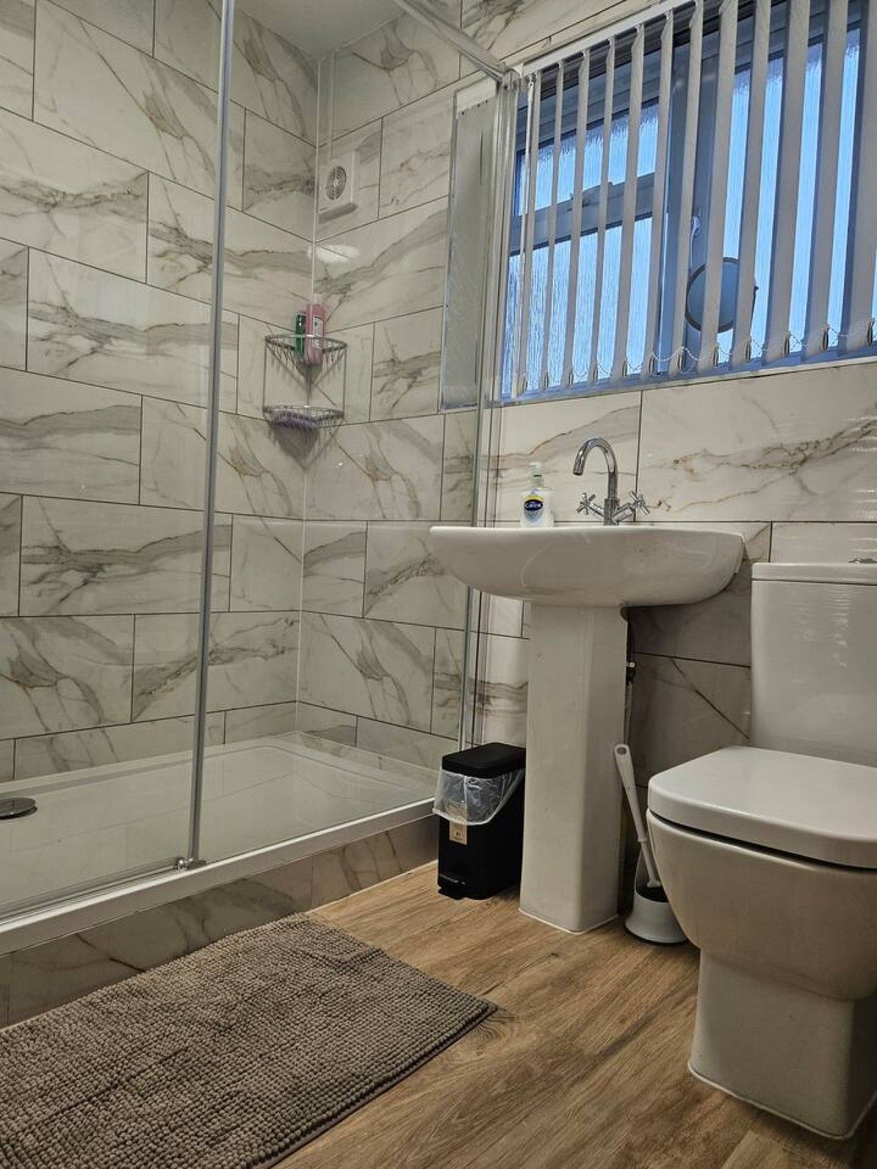 Een badkamer met een douchecabine van glas, een wastafel en een toilet.
