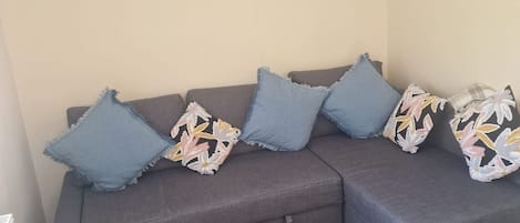 Un sofá gris con cojines azules y estampados florales, un banco de madera y un tapete a rayas.