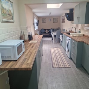 A compact kitchen with a microwave, sink, and washing machine, leading to a dining area with a sofa and table.