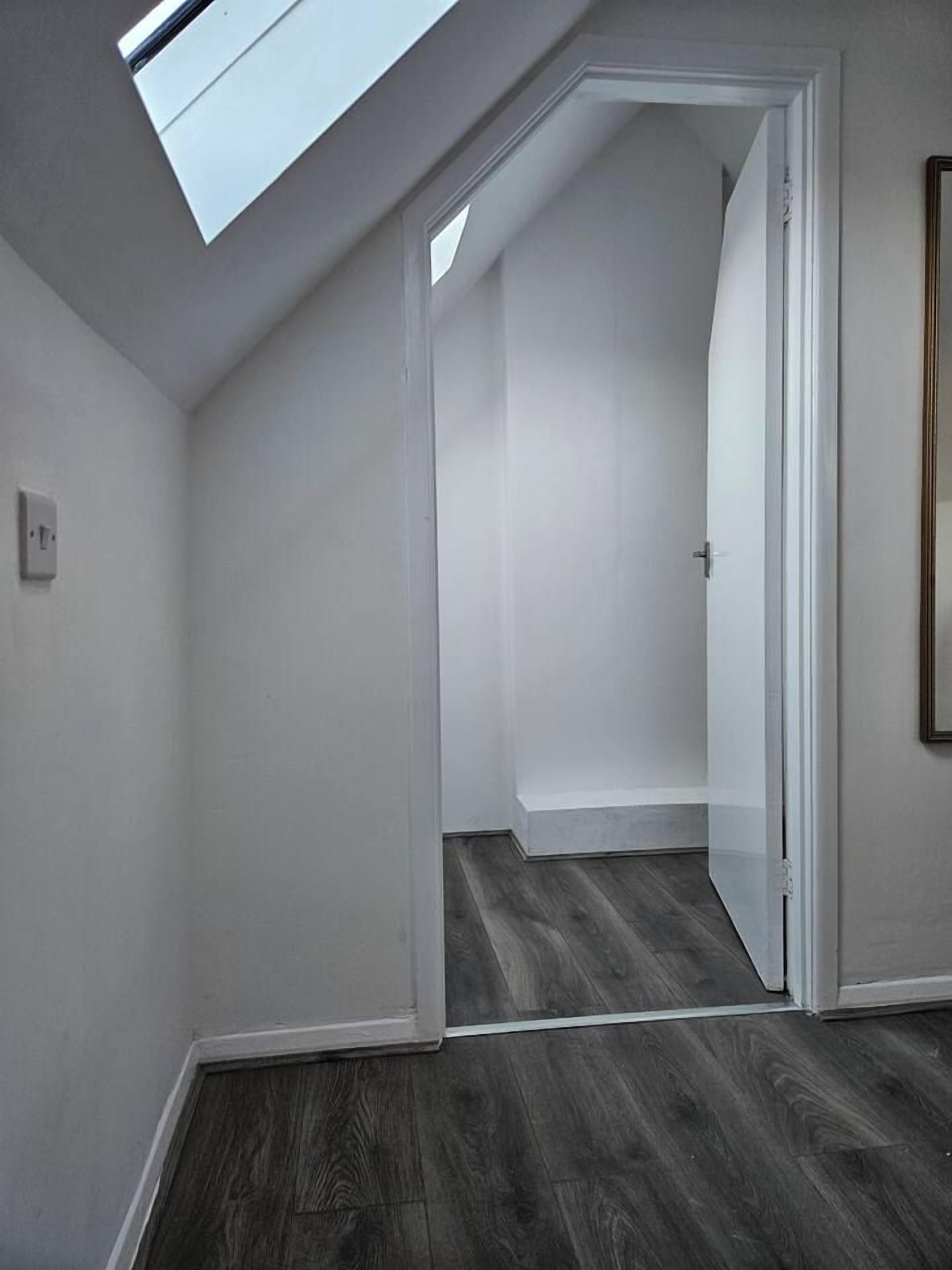 Een kamer met een dakraam, een deur naar een andere kamer en een donker houten vloer.
