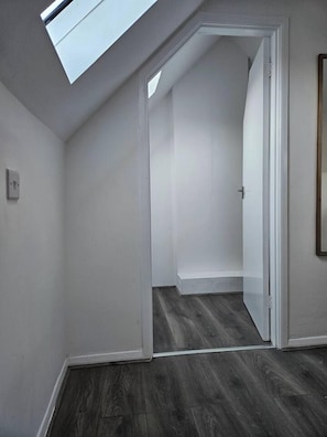 A room with a skylight, a door leading to another room, and a dark wooden floor.