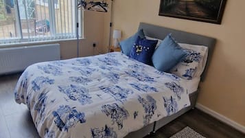 A bedroom with a bed, a painting, a radiator, and a window with blinds.