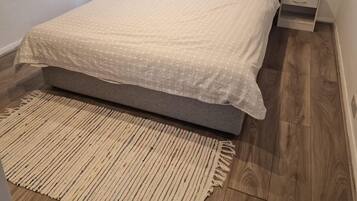 Een slaapkamer met een bed, nachtkastjes, een bedtafel, een raam met jaloezieën en een kamerbreed tapijt met dessin.