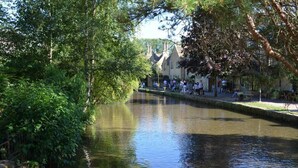 Un fiume tranquillo con un ponte di pietra, alberi e un edificio con persone sedute lungo la riva.