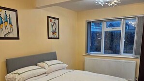 Una camera da letto con un letto, un termosifone, una finestra e due opere d'arte appese al muro.