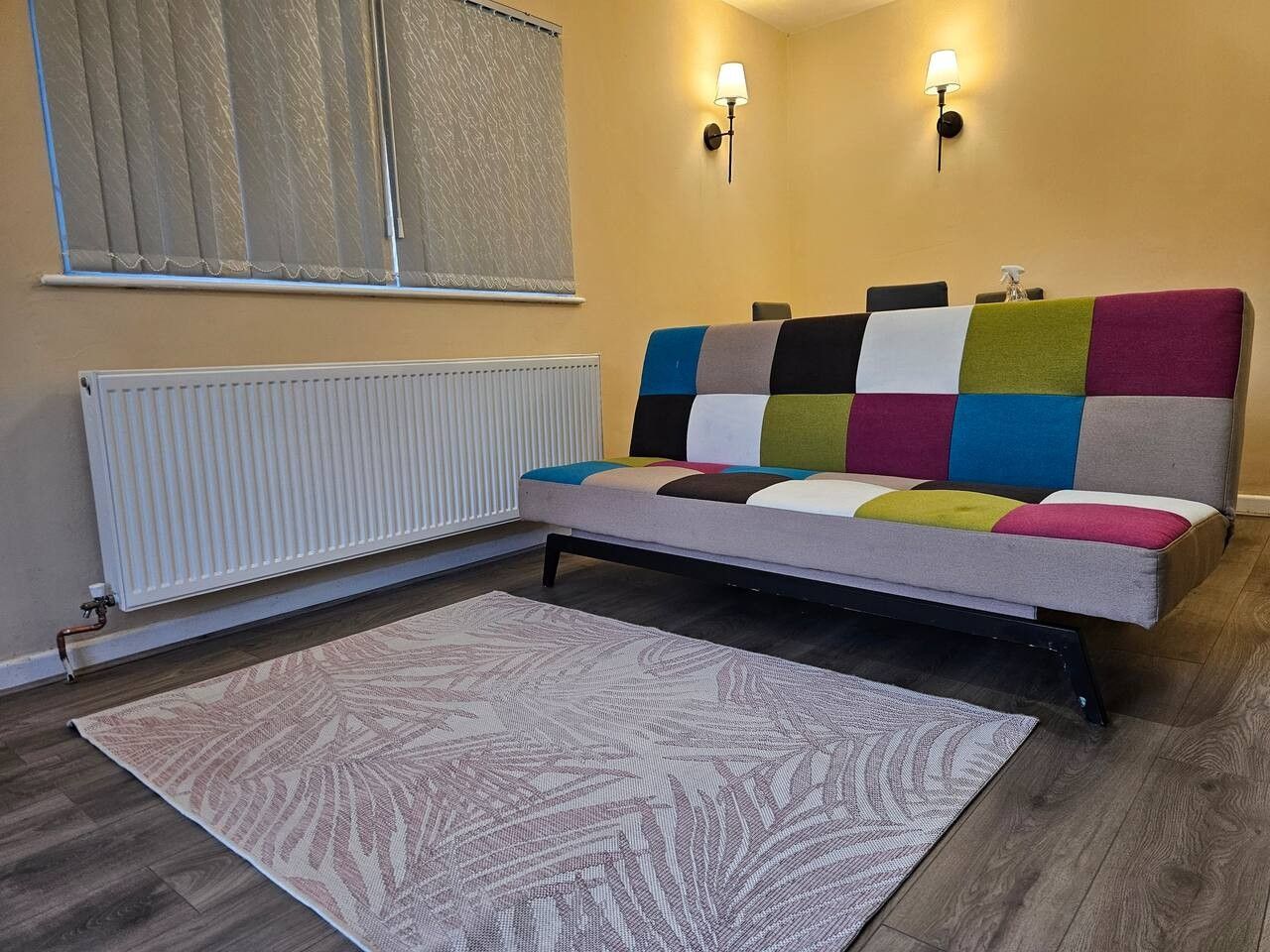 Een kamer met een bed, een radiator, een kamerbreed tapijt met een patroon en twee wandlampen.