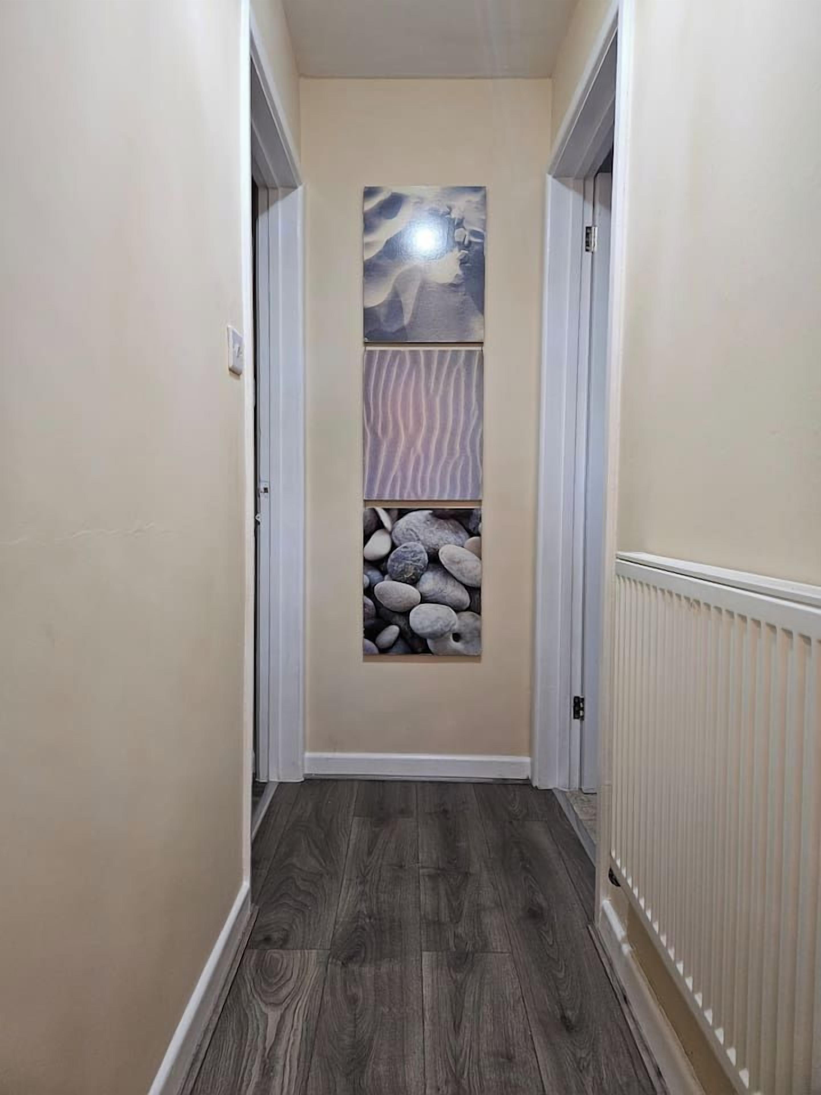 A narrow hallway with a wooden floor, a wall-mounted artwork, and a radiator.