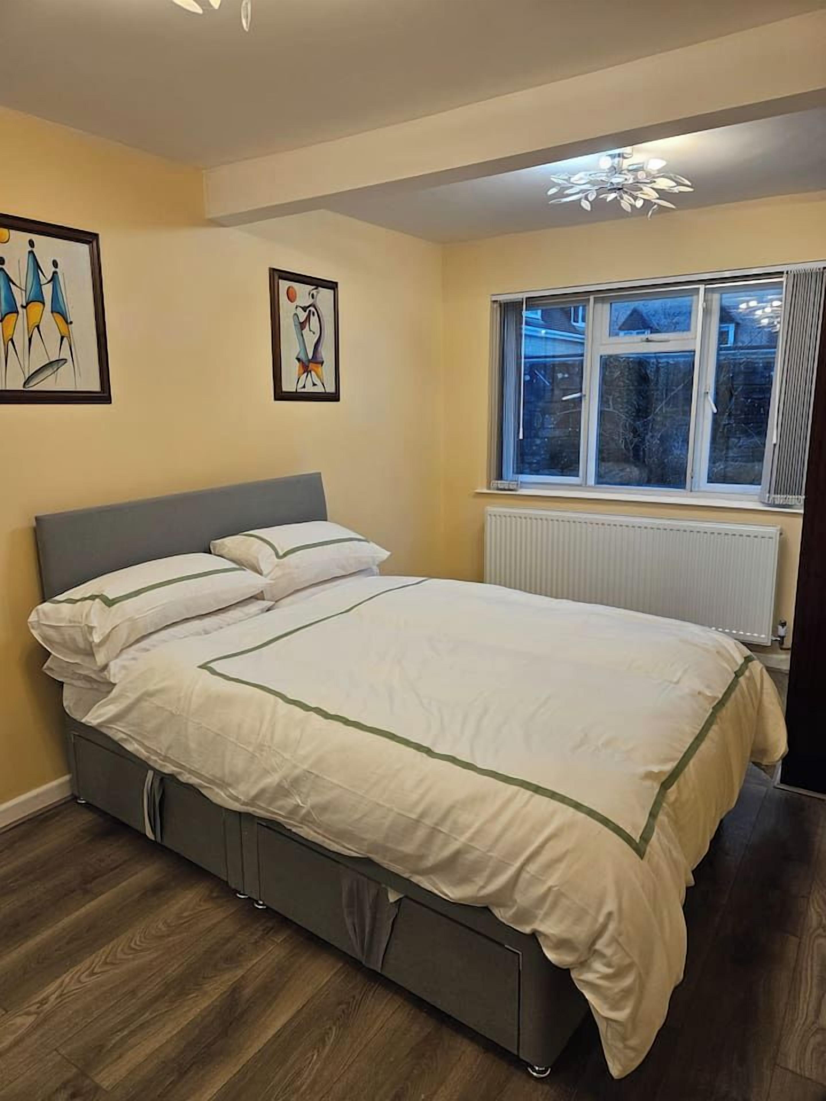 A bedroom with a bed, a radiator, a window, and two framed artworks on the wall.