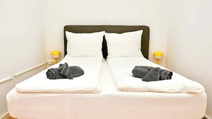 Un letto rifatto con lenzuola bianche e due asciugamani arrotolati sul poggiapiedi.