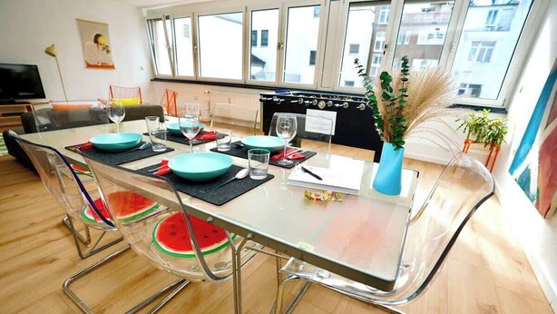 Zona pranzo moderna con tavolo in vetro, sedie in metallo e vista sulla città attraverso ampie finestre.