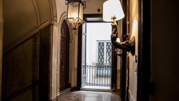 A hallway with patterned flooring, a door leading to a balcony, and wall-mounted lighting fixtures. - Balate maqueda bnb (Palermo)