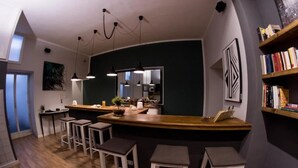 A modern kitchen with a bar area, bar stools, pendant lighting, and a bookshelf. - Balate maqueda bnb (Palermo)