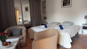 A hotel room with two beds, a sofa, a chair, a table with a vase of flowers, and a lamp. - Gîte Lavande with swimming pool in the heart of Provence with a sensational view! (Saumane-de-Vaucluse)