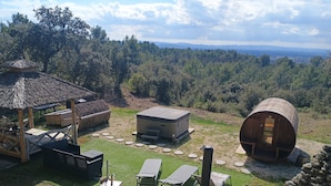 A rustic outdoor setting with a thatched-roof structure, a cylindrical wooden pod, and a small building with a flat roof. - Gîte Lavande with swimming pool in the heart of Provence with a sensational view! (Saumane-de-Vaucluse)