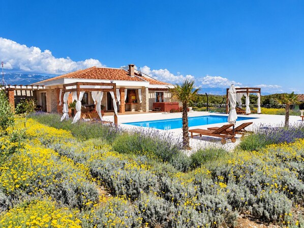 A villa with a swimming pool, outdoor seating, and a garden with yellow flowers.