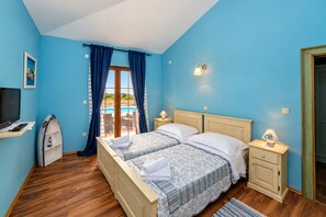 A bedroom with a double bed, a TV, a small desk, and a view of a pool through a glass door.