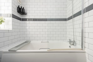 A modern bathroom with white subway tiles, a glass-enclosed bathtub, and a black shelf with toiletries.
