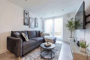 A modern living room with a sofa, a coffee table, and a flat-screen TV mounted on the wall.