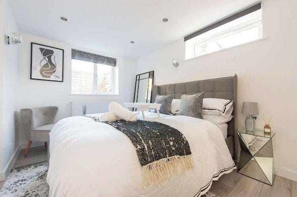 A bedroom with a bed, a chair, a bedside table, a mirror, and a window.
