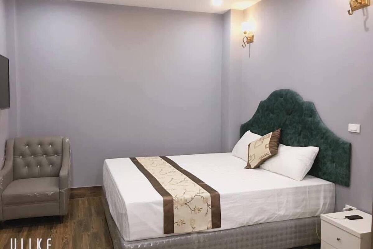 Une chambre à coucher avec un grand lit, une chaise, une table de chevet et un luminaire fixé au mur.