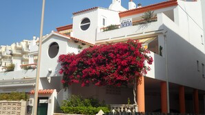 A white building with a red-tiled roof, a circular window, and a sign reading "Costa del Alquila 96 288 80 22".