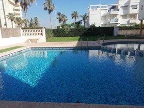 En swimmingpool med krystalklart blåt vand, omgivet af en lav hæk og en belagt terrasse.