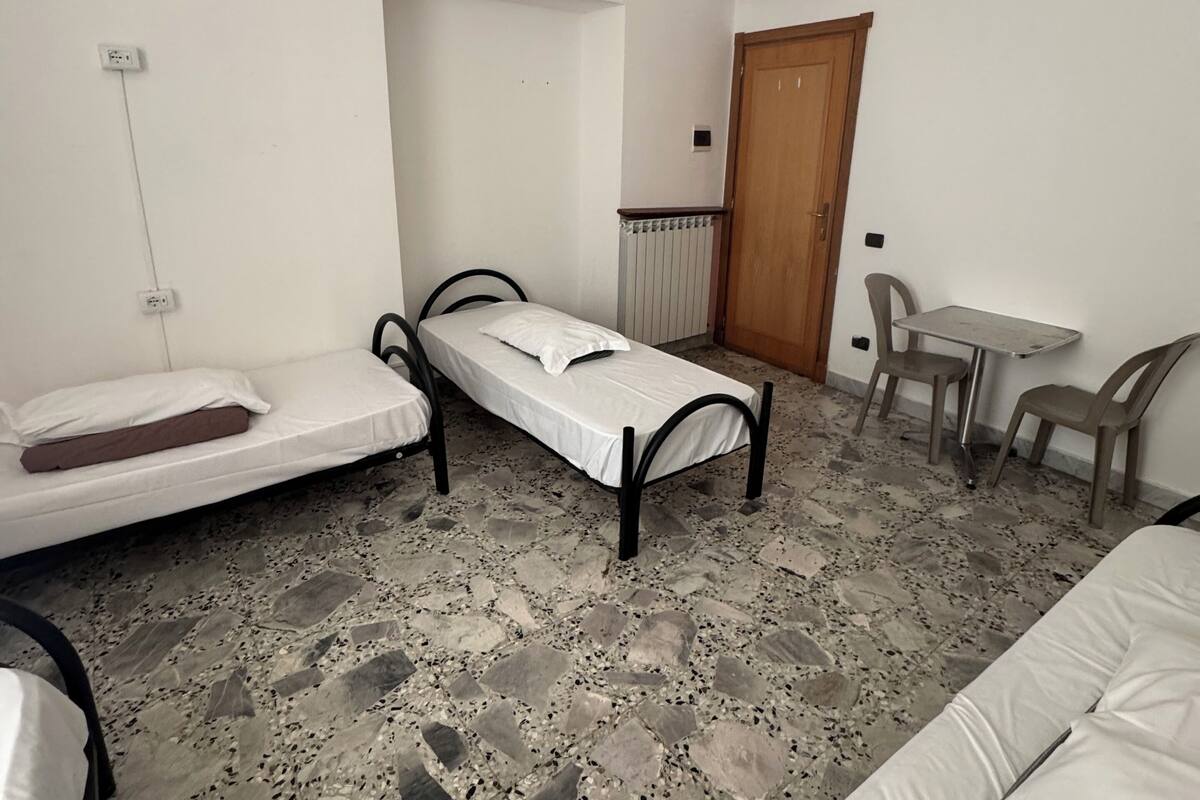 A room with two single beds, a small table with chairs, a radiator, and a door.