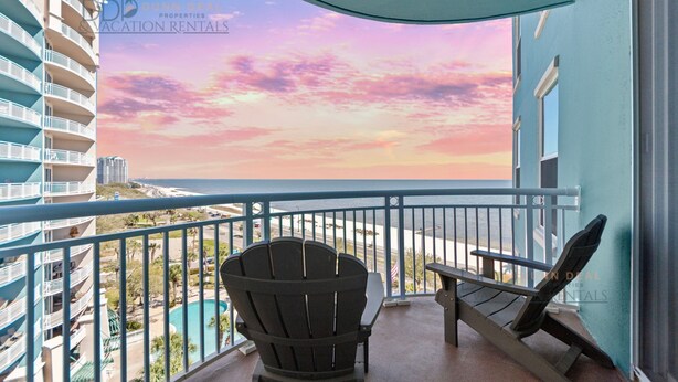Ein Balkon mit Blick auf das Meer und einen Sonnenuntergang. Zwei Adirondack-Stühle und ein kleiner Tisch sind vorhanden.