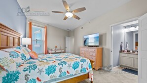 Ein Schlafzimmer mit Bett, Deckenventilator, Fernseher, Schminktisch und einem Badezimmer mit Spiegel und Waschbecken.