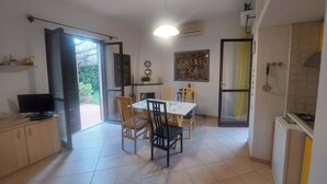 A compact kitchen with a dining area, a TV, and a ceiling fan. - Apartment Cala Azzurra - with large garden and a stone's throw from the sea (Cavo)