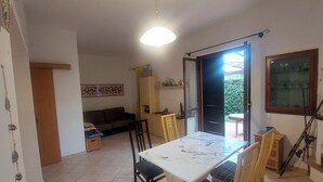 A dining area with a marble table and chairs, a sofa, and a door leading outside. - Apartment Cala Azzurra - with large garden and a stone's throw from the sea (Cavo)