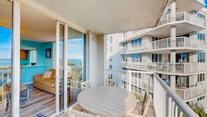 Un balcón con mesa y sillas, un sofá y vistas a un edificio con balcones.