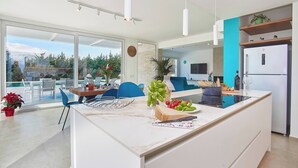 Una cocina moderna con una isla grande, un comedor con sillas azules y vistas al exterior.
